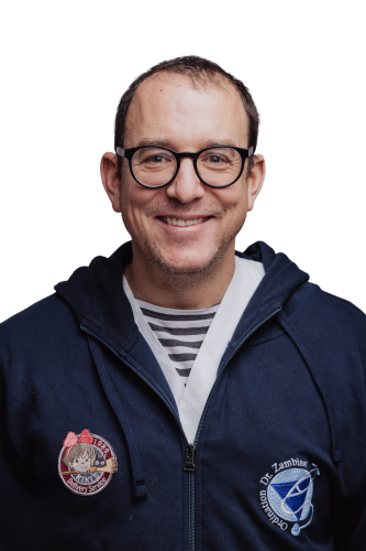 Dr. med. univ. Markus Zambisi, ein Lächelnder Mann mit Brille und Kiki's Lieferservice Stickerei und Firmenlogo.